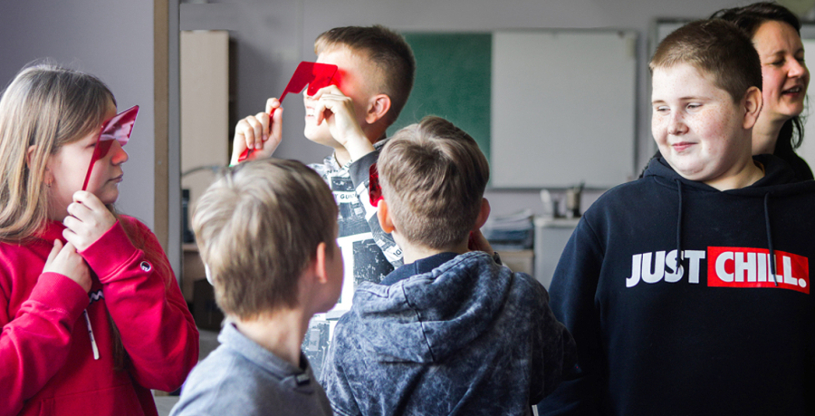 Attēlā redzami pieci 5. klases skolēni - meitenes un zēni. Divi no viņiem pie acīm ir pielikuši lielas sarkanas brilles. Vienam zēnam uz džempera ir uzraksts 